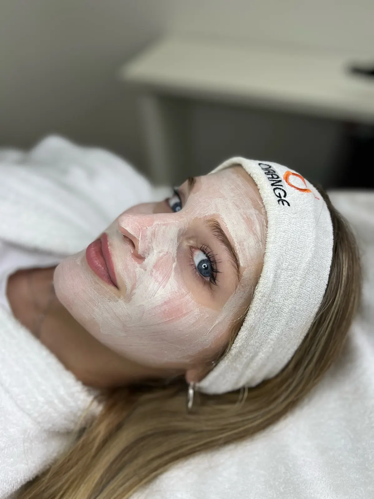 Clienta recostada con máscara facial y vincha de Orange durante una higiene facial